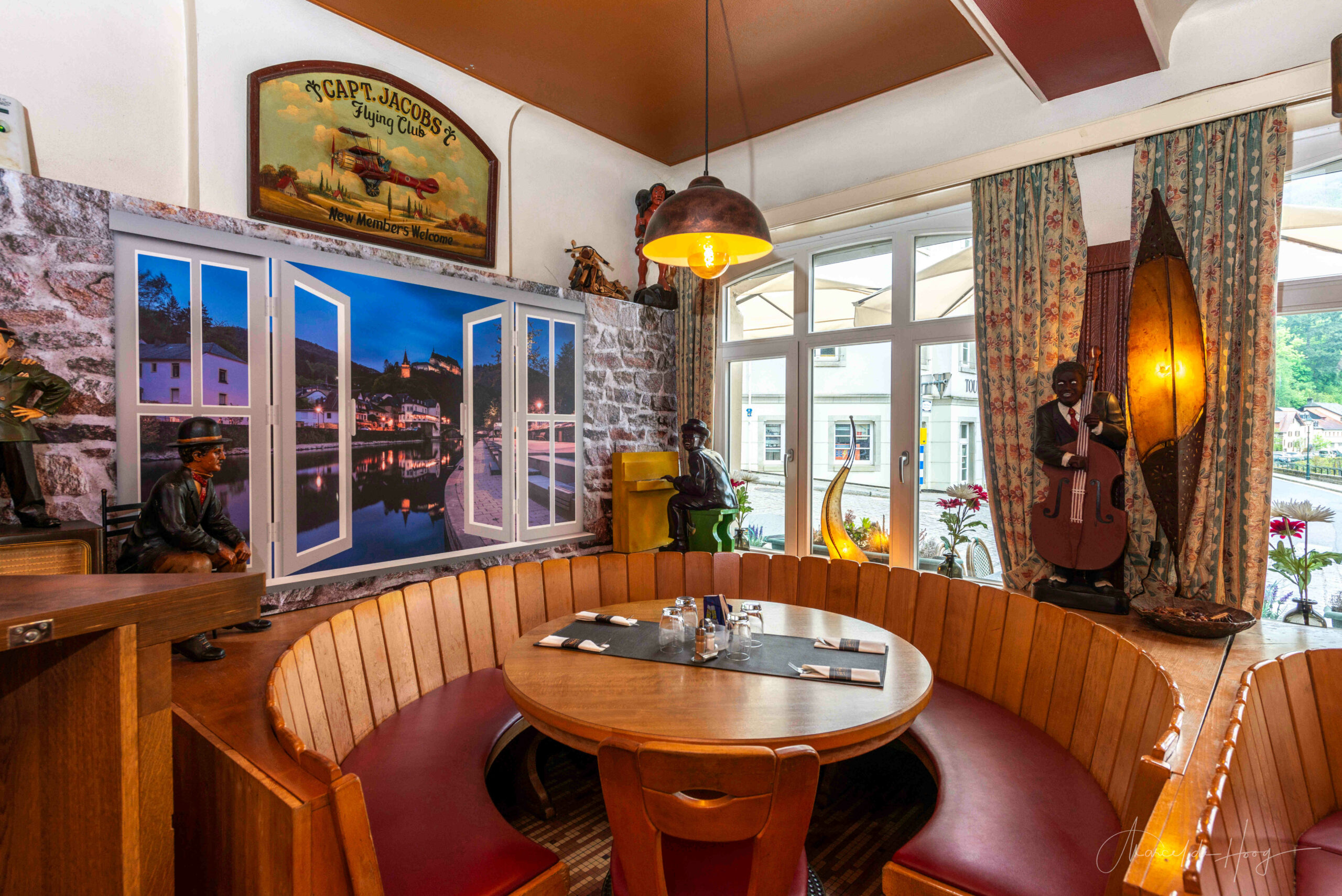 Cozy circular seating area by the window at Café Du Pont in Vianden, captured by Marcel de Hoog.
